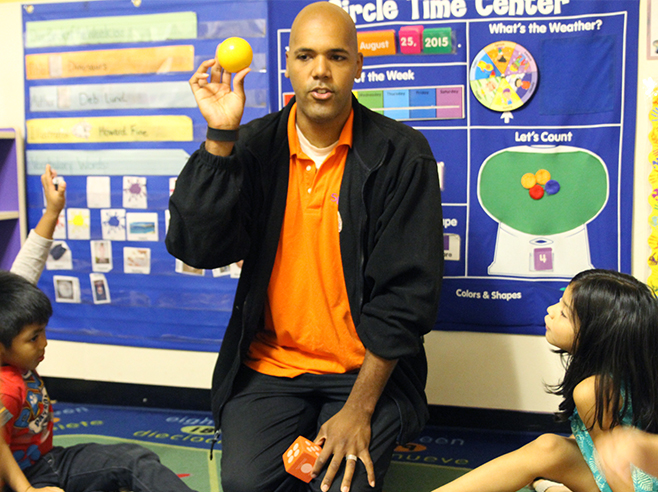 Teacher holds up a ball and students raise their hands.