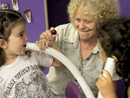 Students hold each end of a plastic tube. One talks into one end, while the other listens.