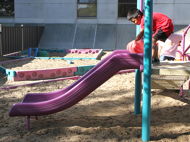 Student rolls a ball down a slide in a playground.
