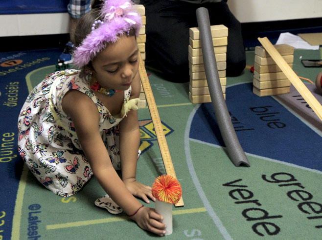 A student sets up an obstacle, a cardboard tube with a pompom ball on top, at the base of one of three different ramps.