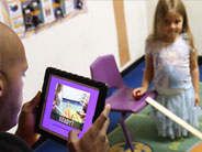 Teacher uses an iPad to record a student about to roll a marble down a ramp.