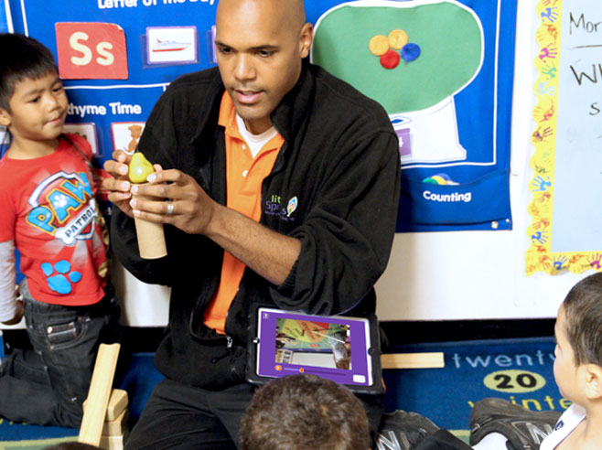 As students look on, teacher creates an obstacle out of a toy pear and a cardboard tube.