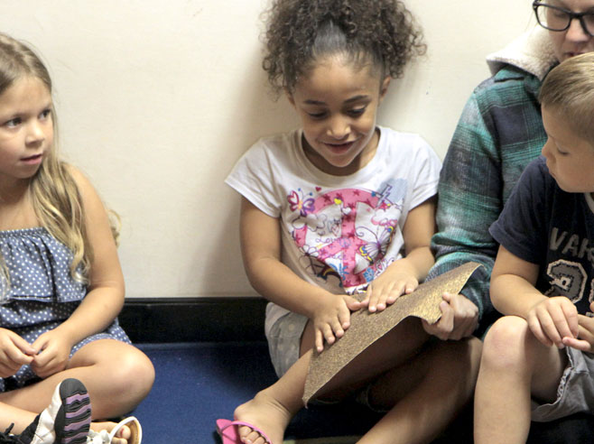 A seated student feels a piece of sand-paper as other students and a teacher look on.