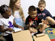 Two students are rolling cardboard tubes down two differently sloping cardboard ramps.