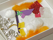 A cardboard box lid filled with a collage of materials of different textures and colors.