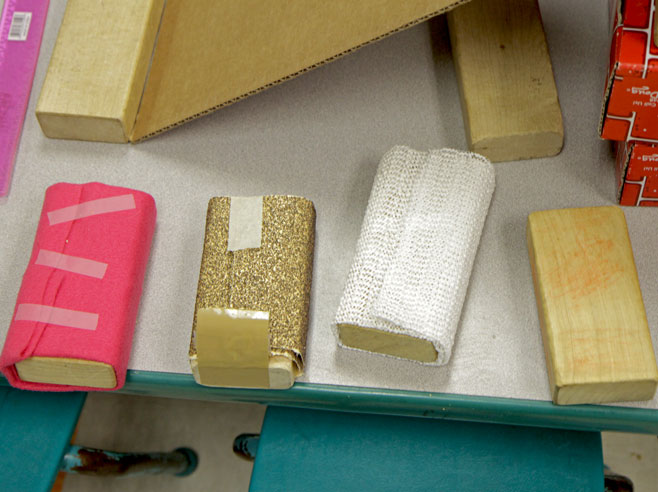 Four blocks, each covered in a different textured material, sit on a table.