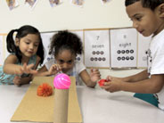 Students send objects down a ramp setup toward an obstacle.