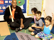 Students cheer and point after an object has gone down a cardboard ramp that they are sitting next to.
