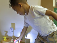 Toy objects placed in front of a spot lit wall create shadows. A student in the foreground reaches to move an object.