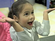 A student smiles and holds her arms up in a shrugging gesture.