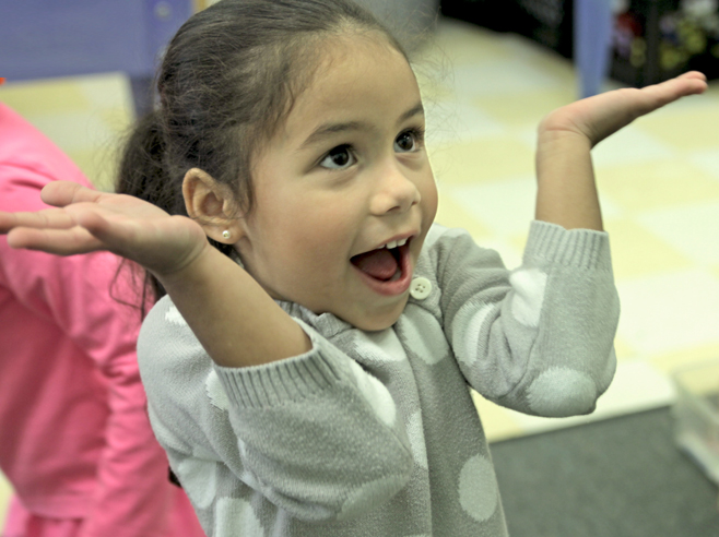 A student smiles and holds her arms up in a shrugging gesture.
