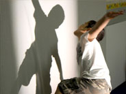A student dances, and watches his shadow move, on a white wall in front of him.