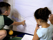 Two students look at concentrically circular outlines drawn on a piece of poster-board. One student points at the lines.