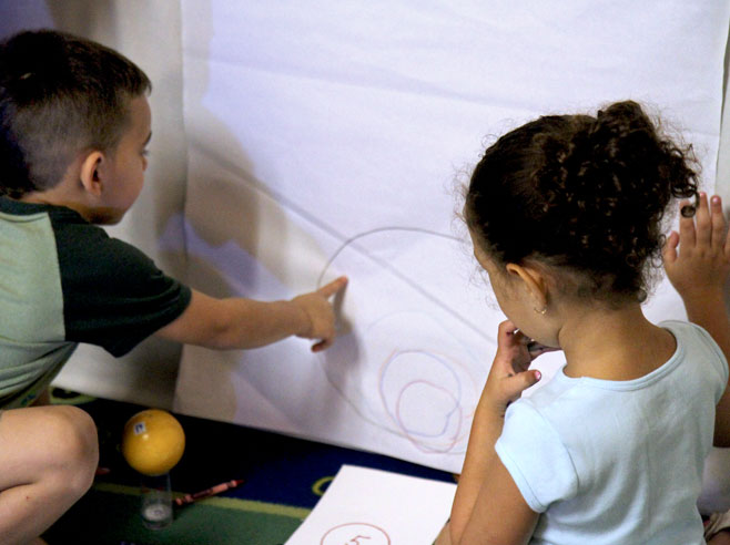 Two students look at concentrically circular outlines drawn on a piece of poster-board. One student points at the lines.