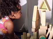 A student is looking at the wall behind a structure of wooden blocks of different shapes, and colors.