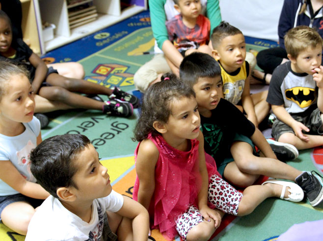 A group of students are seated on the floor watching something out of view.