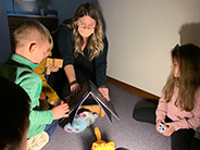 Light shining on teacher covering stuffed animal with a book. Two students watching.